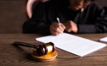 A person signing a document with a judge hammer in the foreground.