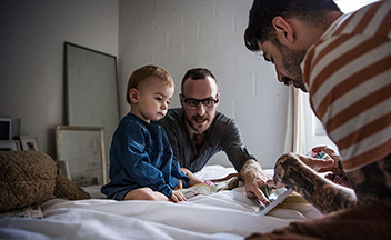 Two men with young child on bed