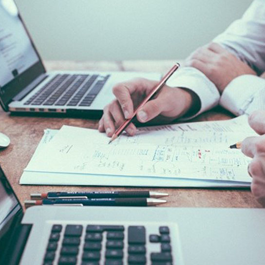 Close up of people in an office using laptop and writing