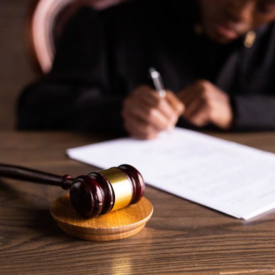 A person signing a document with a judge hammer in the foreground.