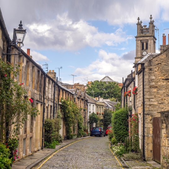 Street photo in Edinburgh, lined on both sides with houses and a church in the distance