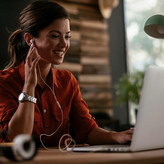 Image of a woman sat at a desk on a laptop, wearing headphones