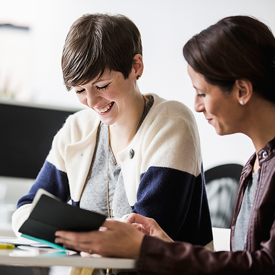 Two women sat together in office smiling