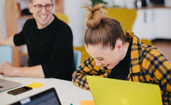 Young woman laughing with colleague using a laptop