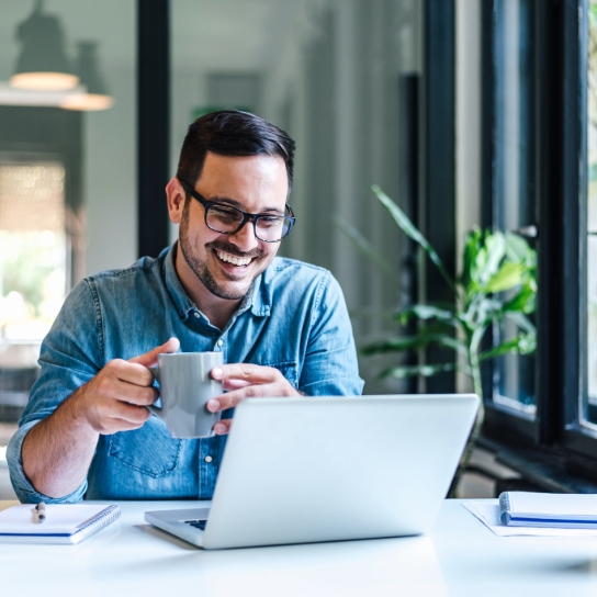 Man in shirt holding a mug looking at a laptop