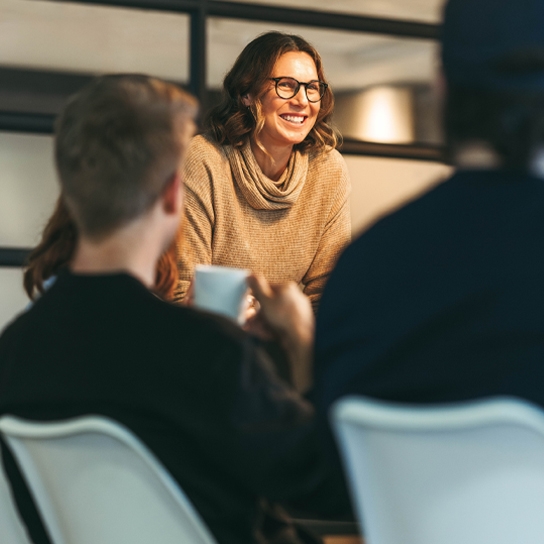 Photo of lady in an office setting, smiling at her colleagues who are seated
