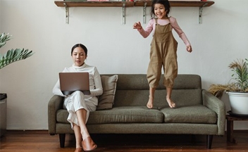 Parent on laptop with child on sofa