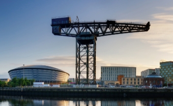 Cityscape photo in Glasgow, featuring office buildings and a large crane at sunset