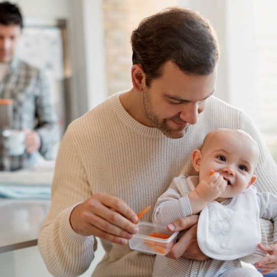 Family in kitchen with baby eating a snack of sliced carrots