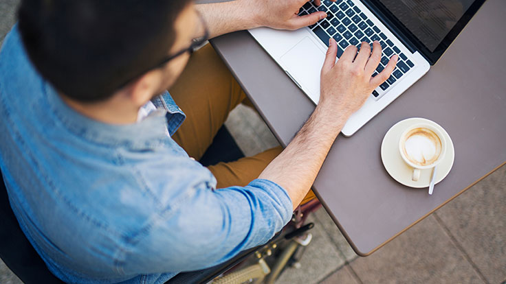 Close up of man using laptop with coffee