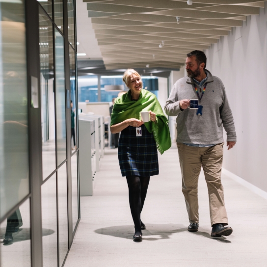 RSA colleagues walking down corridor together in office, holding cups of coffee and smiling.
