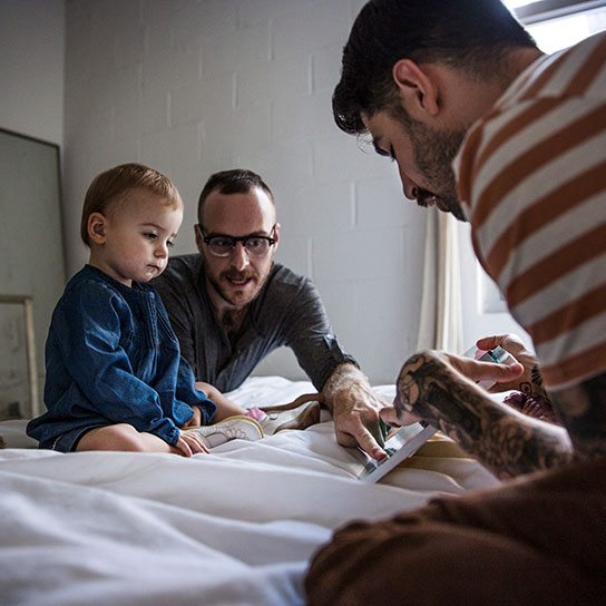 Two men with young child on bed